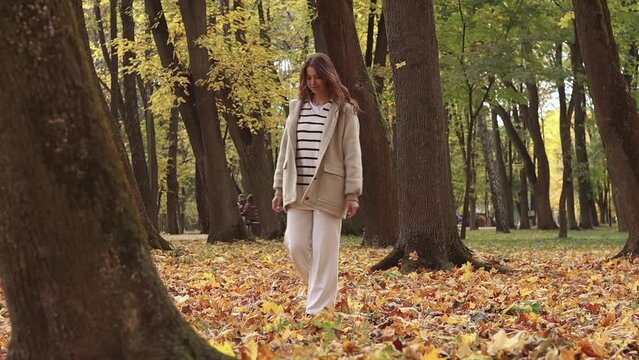 Woman walking outdoor, young european lady in warm sunny autumn city park season, fall, hold yellow orange red leaves, lifestyle, spending free time

