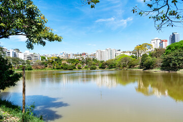 Residential buildings on the edge of a lake with many trees. Blue sky with clouds. City of Belo Horizonte. Brazil