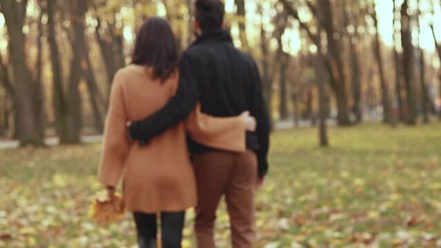 Heterosexual caucasian young loving couple walking outside in the city park sunny weather, hugging smiling kissing laughing spending time together. Autumn, fall season, orange yellow red maple leaves

