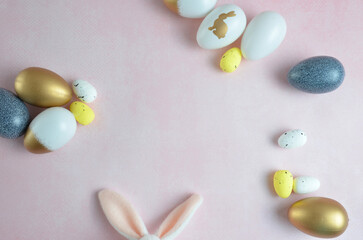 Eggs of gold and blue colors with the Easter bunny. Bunny ears. Happy easter. Pink background.