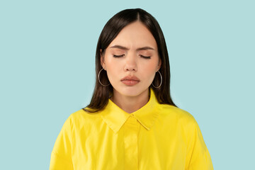 Upset emotional young woman, with eyes closed showing a vulnerable moment of sadness at blue studio...