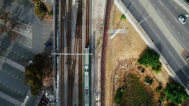 A solitary cyclist travels beside a railway line, captured from above in a birds eye perspective, contrasting with the linear patterns of tracks and pavement.
