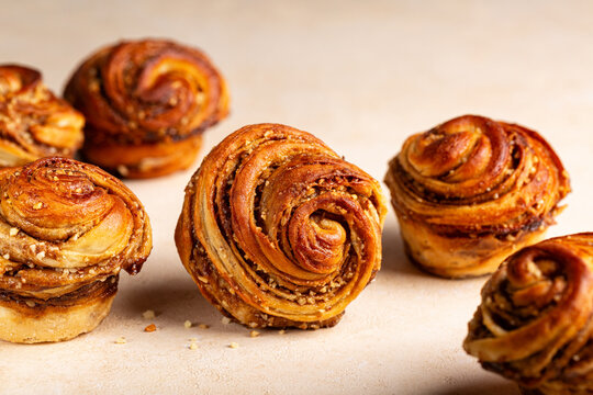 Homemade cruffins, a hybrid of a croissant and a muffin, filled with mix of butter, brown sugar and nuts. Baked in a muffin mould. Light beige table surface.