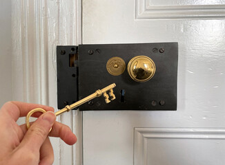 Antique door lock. Golden door handle with antique gold-engraved crest. Ancient lock with key. Old metal key in the keyhole. Hand holding the key.