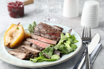 Delicious roasted beef meat served with caramelized pear and greens on light table, closeup