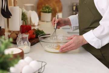 Woman whisking eggs in bowl at light table indoors, closeup