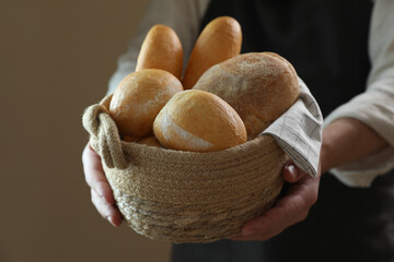 Man holding wicker basket with different types of bread on brown background, closeup