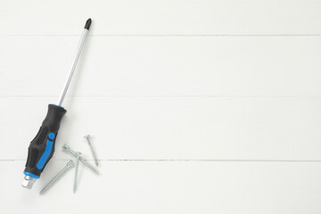 Screwdriver with black handle and screws on white wooden table, flat lay. Space for text