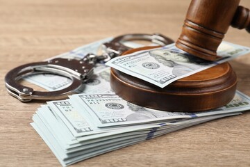 Judge's gavel, money and handcuffs on wooden table, closeup