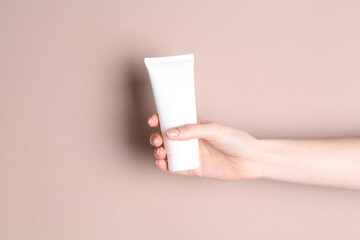 Woman with tube of cream on beige background, closeup