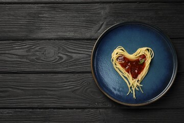 Heart made with spaghetti and sauce on black wooden table, top view. Space for text