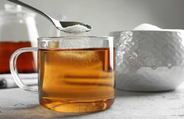 Adding sugar into cup of tea at grey textured table, closeup
