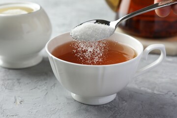 Adding sugar into cup of tea at grey textured table, closeup