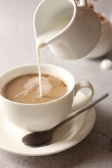 Pouring milk into cup with coffee on light grey textured table, closeup