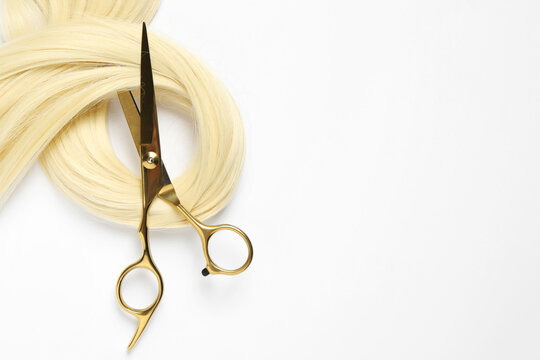 Professional hairdresser scissors with blonde hair strand on white background, top view