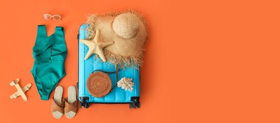 Suitcase with beach accessories on orange background with space for text
