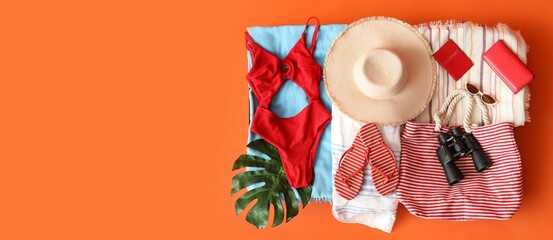 Open suitcase with beach accessories and clothes on orange background with space for text