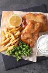 Tasty fish, chips, sauce and peas on grey table, top view