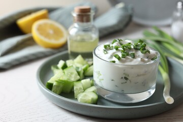 Delicious yogurt, green onion and cucumbers on white wooden table, closeup