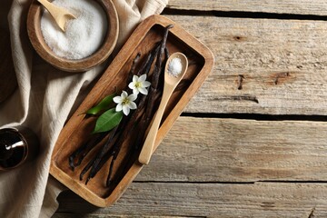 Vanilla pods, flowers, leaves and sugar on wooden table, top view. Space for text