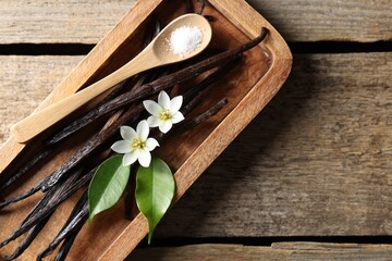 Vanilla pods, flowers, leaves and spoon with sugar on wooden table, top view