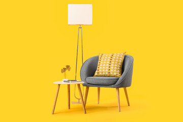 Cozy grey armchair with cushion, standard lamp and coffee table on yellow background