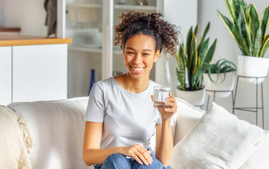 Healthy lifestyle concept. Beautiful young Afro American woman holding a glass of clean water...