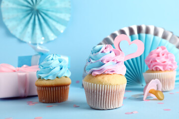 Delicious cupcakes with gift boxes, pacifier and decor on blue background. Gender reveal party...
