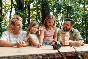 Young playful family is playing fun jenga board game in nature.