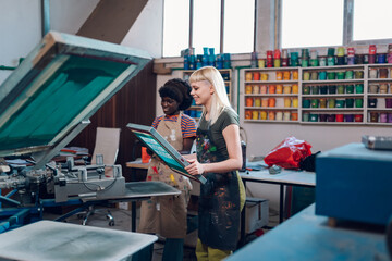 Print shop worker putting plate on machine and interracial supervisor watching