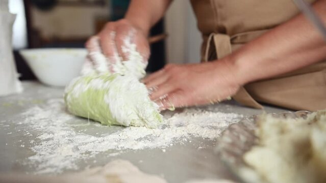 Close-up woman's hands making sourdough dough with green spinach for ravioli in a rustic home kitchen. Housewife kneading dough for preparing homemade bread. Bakery. Culinary. Traditional cuisine