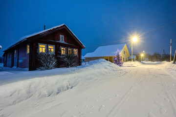 Electric light in windows of rural house in snowy evening village on Christmas Eve in northern Europe.