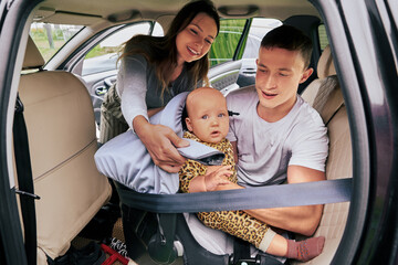 Parents tighten harness security of car seat across his baby body.