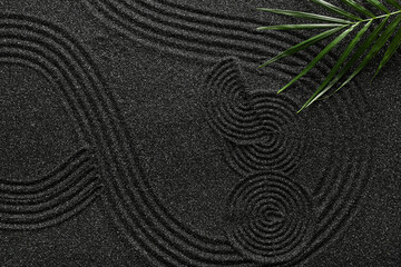 Palm leaf on black sand with lines. Zen concept
