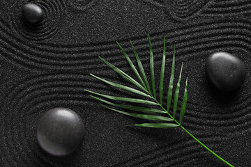 Spa stones on black sand with lines and palm leaf. Zen concept