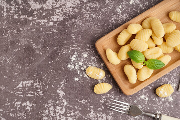 Wooden board with tasty gnocchi and basil on grunge background
