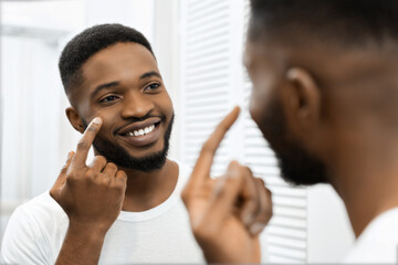 Man smiling applying face cream in mirror in bathroom