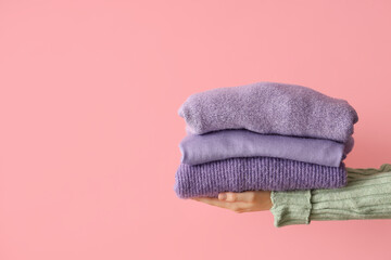 Woman with folded sweaters on pink background
