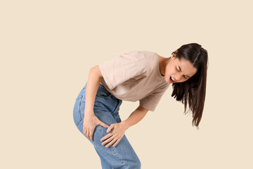 Young woman suffering from leg pain on beige background