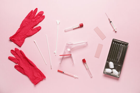 Medical gloves with gynecological speculum, pap smear test tools and tubes on pink background
