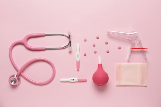 Stethoscope with gynecological speculum, pills and pregnancy tests on pink background