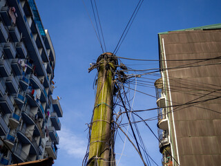 Many wires are piled on a wooden pole in a modern city. Electrification of an Asian city. Vintage...