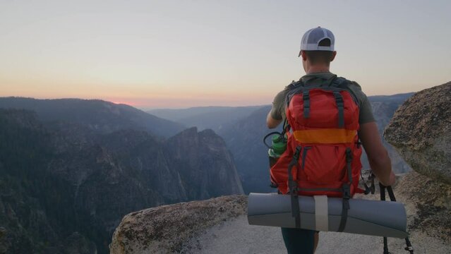 Handsome young athletic blogger wit red backpack and trekking poles reaches the summit of mountain range in Yosemite national park in summer at sunset. High quality 4k footage