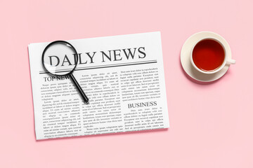 Newspaper with magnifying glass and cup of tea on pink background