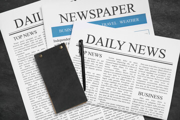 Newspapers with notebook and pen on black grunge background