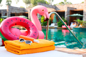 Beach accessories on sun lounger, inflatable ring and float near outdoor swimming pool at luxury resort, space for text