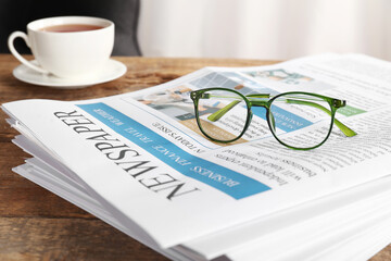 Stack of newspapers with cup of tea and eyeglasses on wooden table in office