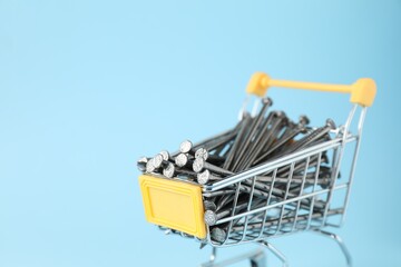 Metal nails in shopping cart on light blue background, closeup. Space for text