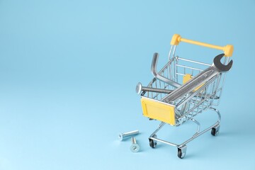 Different construction tools in shopping cart on light blue background, space for text