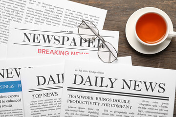 Newspapers with cup of tea and eyeglasses on wooden background